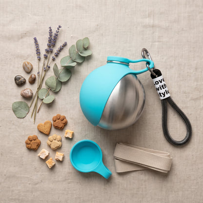 Portable Dog Water Dispenser in teal, flat lay with lavender, eucalyptus, treats, collapsible cup and leash strap